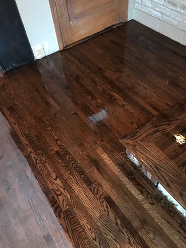 In-progress hardwood kitchen floor staining and finishing with warm, dark-colored stain.