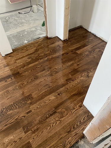 Recently stained and finished hardwood hallway floor with dark and varied stain.