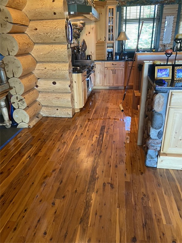 Recently stained and finished hardwood kitchen floor in log cabin with narrow floor boards.