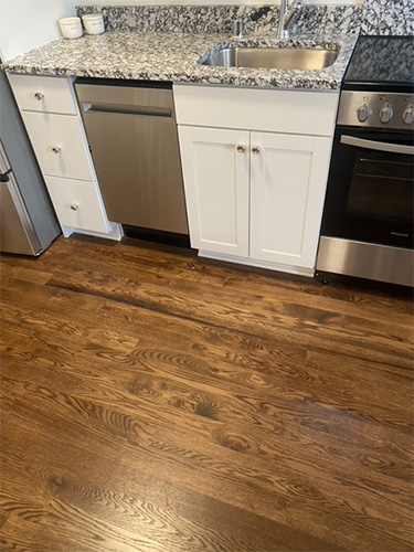 Freshly stained and finished hardwood kitchen floor in dark stain against white cabinets.