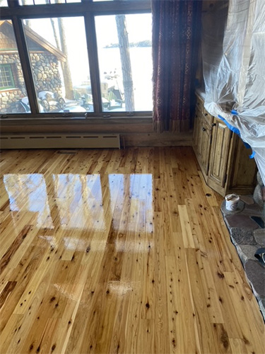 Recently stained and finished hardwood family room floor with honey-colored stain in front of fireplace.