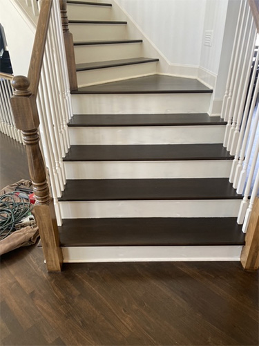 Recently stained and finished hardwood staircase with odd angles and very dark stain showing bottom step.