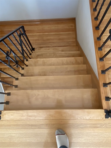 Freshly stained and finished hardwood staircase with light stain showing top step looking down.